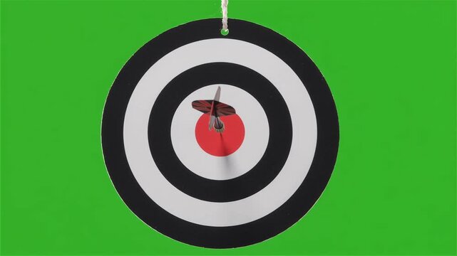 Dart flies into frame and hits the center bullseye of a hanging target, green screen background