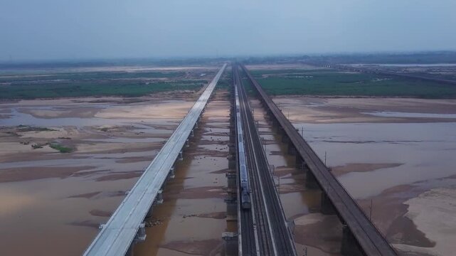 Aerial view of parallel railway bridge spanning wide river floodplain with sandy banks and green agricultural fields in Dehri on Sone, Bihar, India during monsoon season.