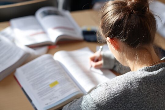 Over shoulder view of student sitting study desk highlighting important point textbook writing summary notebook notebook stationery visible quiet study environment camera behind subject no face