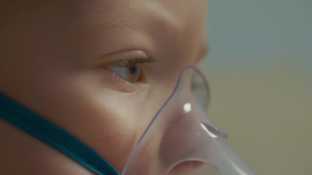 Close-up of a child using a mask connected to a nebulizer. The child inhales a saline solution to help with cough and respiratory issues at home.
