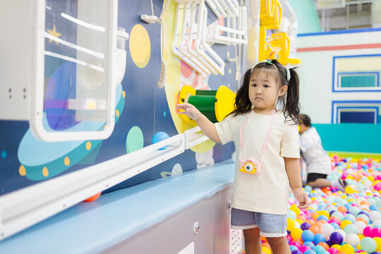 Little girl playing with interactive wall game in indoor playground,A cute young Asian girl in a cream t-shirt and denim shorts explores a space-themed interactive science wall at a colorful indoor.