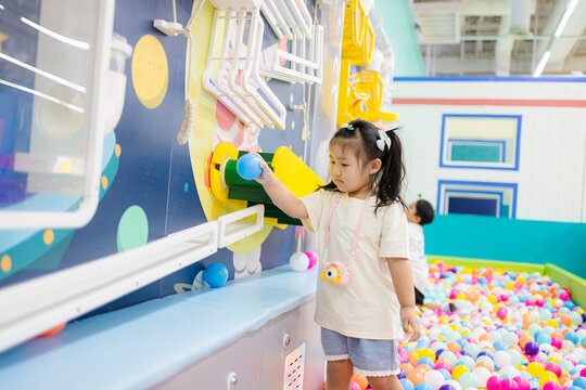 Little girl playing with interactive wall game in indoor playground,A cute young Asian girl in a cream t-shirt and denim shorts explores a space-themed interactive science wall at a colorful indoor.