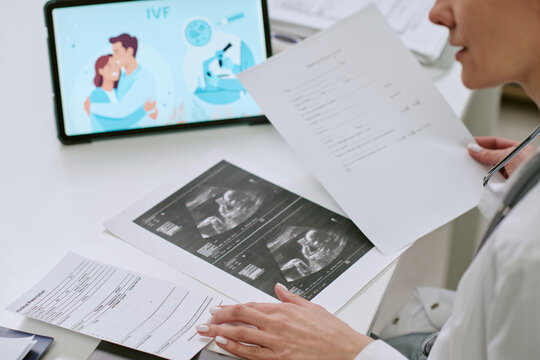 Over shoulder view of middle aged woman reviewing ultrasound printouts and IVF paperwork during fertility consultation