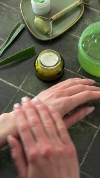 Close up of woman dipping finger into cosmetic jar and applying cream on her hand, skincare routine on dark background.