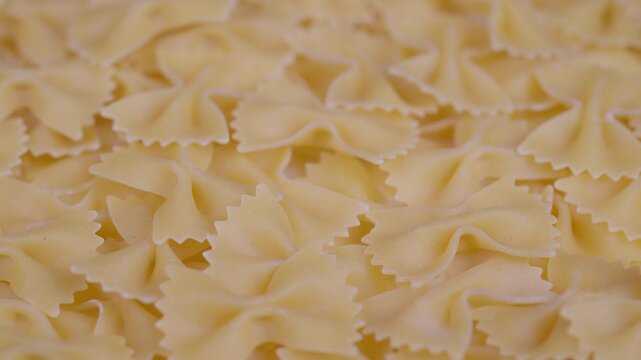Farfalle pasta pieces with matte finish. Closeup of raw farfalle pasta arranged on surface. Detailed view of uncooked farfalle pasta with textured edges under warm lighting