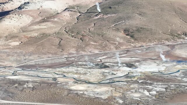 Cinematic flying forward over the steaming geothermal vents and colorful mineral deposits of El Tatio at dawn, high in the Chilean Altiplano
