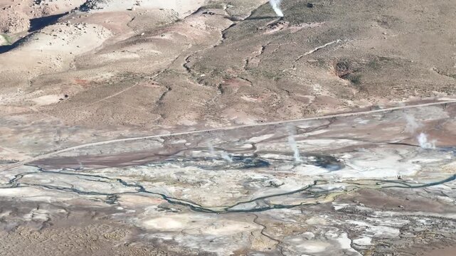 Cinematic aerial flying sideways to the right across the steaming El Tatio geyser field, revealing colorful mineral deposits and the volcanic landscape of the Chilean Altiplano