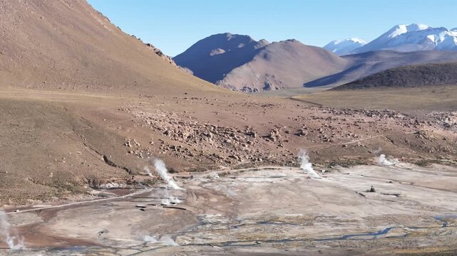 Cinematic aerial pulling back from steaming geothermal vents to reveal the vast El Tatio geyser field nestled among the volcanic peaks of the Chilean Altiplano