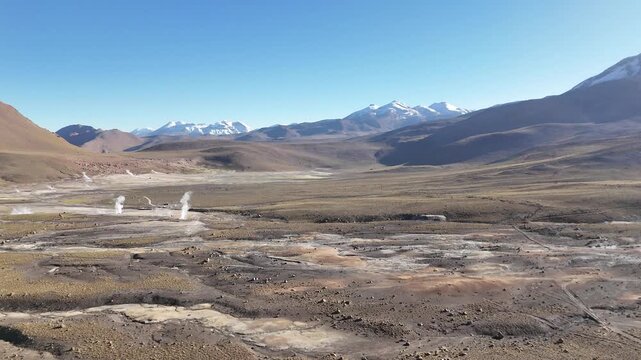 Cinematic aerial flying forward over steaming geothermal vents and colorful mineral runoff at El Tatio, revealing the vast volcanic plateau of the Chilean Altiplano