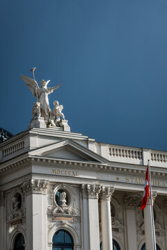 Zurich, Switzerland - 02 April 2023: View of the Schauspielhaus, its elegant facade adorned with sculptures under a deep blue sky, a Swiss flag gently waving.