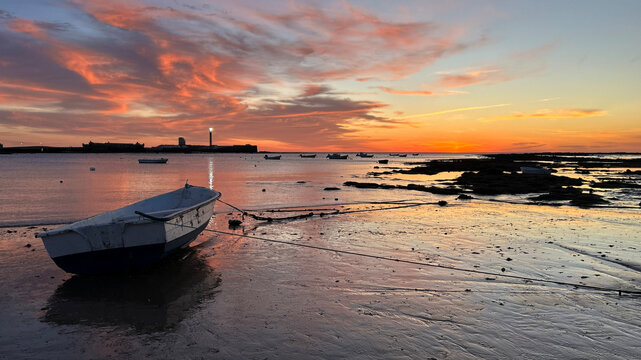 Un'incantevole vista di una barca tradizionale sulla sabbia umida durante un tramonto infuocato. I colori vivaci del cielo si riflettono sulla costa, creando un'atmosfera serena e magica in una locali
