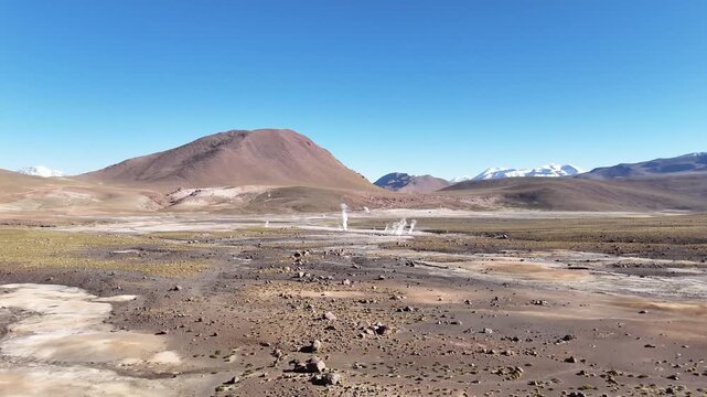 Cinematic aerial flying forward over steaming geothermal vents and colorful mineral runoff at El Tatio, revealing the vast volcanic plateau of the Chilean Altiplano