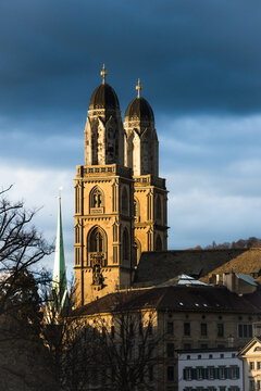 Zurich, Switzerland - 02 April 2023: View of the majestic Grossmunster church towers piercing the skyline, its sandstone facade glowing warmly against the dramatic backdrop of a stormy sky.