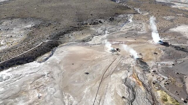 Cinematic flying forward over the steaming geothermal vents and colorful mineral deposits of El Tatio at dawn, high in the Chilean Altiplano