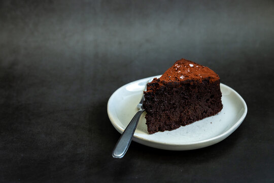 Flourless chocolate cake sprinkled with salt on a white plate with dark backdrop