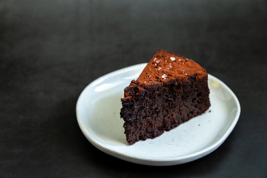Flourless chocolate cake sprinkled with salt on a white plate with dark backdrop