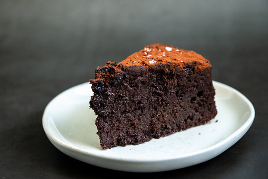 Flourless chocolate cake sprinkled with salt on a white plate with dark backdrop