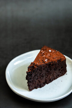 Flourless chocolate cake sprinkled with salt on a white plate with dark backdrop
