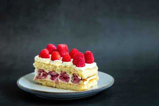 Yellow cake with raspberries and cream on a plate with a dark backdrop