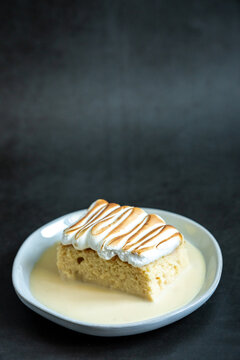 Slice of tres leches cake on a white plate and dark backdrop