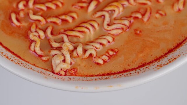 Closeup of fiery ramen in broth. Overhead shot of spicy noodle soup with oil droplets. Glistening instant ramen noodles immersed in vibrant orangered soup with steam