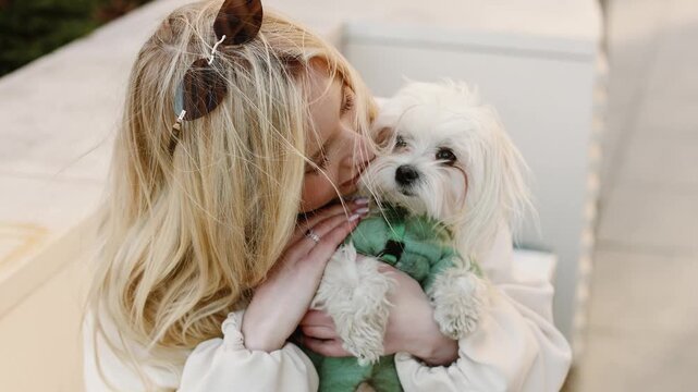4K slow motion close up of young woman hugging and kissing cute white Maltese dog, tender emotional moment, pet love, care and affection, lifestyle portrait outdoors, soft natural light