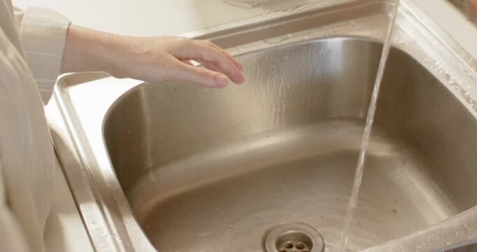 Woman washing potato under running faucet at kitchen sink, scrubbing for meal prep with smartwatch