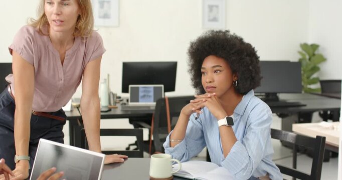 Diverse team at table in business, leader leaning presenter showing laptop swatches deciding colors