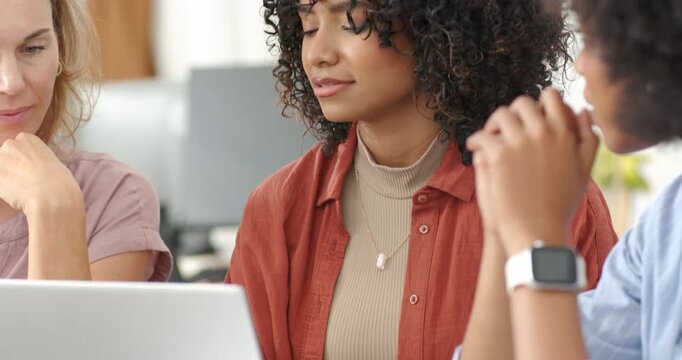 Diverse female coworkers reviewing draft on silver laptop, central woman typing while team smiling