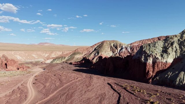 Cinematic aerial flying forward over the winding desert tracks and vibrant mineral-rich ridges of Valle del Arcoiris (Rainbow Valley) near San Pedro de Atacama, Chile