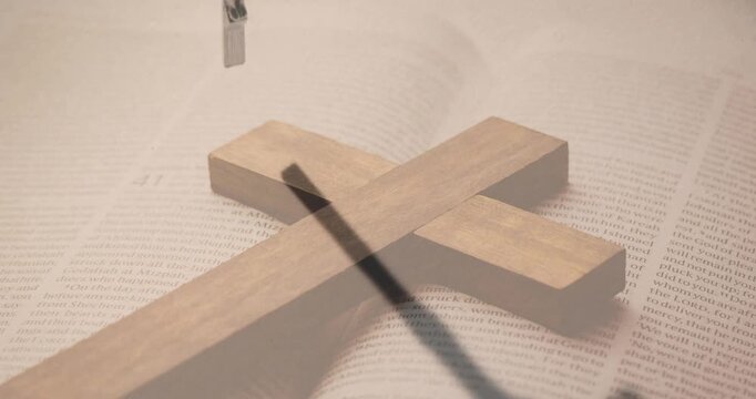 Wooden cross lying on book, descending metal crucifix entering frame casting long shadow for faith
