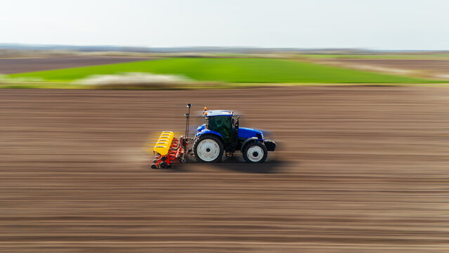 Aerial view of a tractor speeding across the vast, freshly tilled field, contrasting with vibrant green patches in the distance, Sremska Mitrovica, Vojvodina, Serbia.