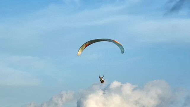 Two people enjoying thrilling tandem paragliding against a bright blue sky, experiencing adventure and freedom while soaring high in white clouds. Aerial view drone flight