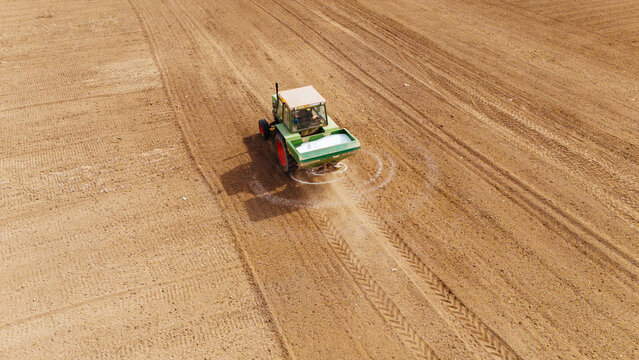 Aerial view of a tractor spreading fertilizer over a field, casting a shadow on the dry, furrowed earth, Sremska Mitrovica, Vojvodina, Serbia.