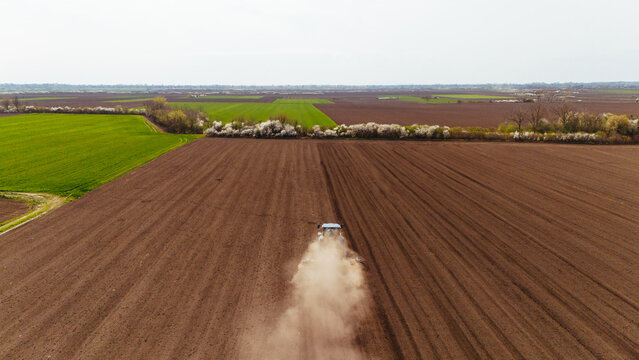 Aerial view of tractor working the rich, dark soil contrasts with vibrant green fields, creating a patchwork landscape, Sremska Mitrovica, Vojvodina, Serbia.