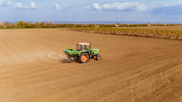 Aerial view of a tractor meticulously spreading fertilizer across the vast expanse of a field, creating a stark contrast with the sky, Sremska Mitrovica, Vojvodina, Serbia.