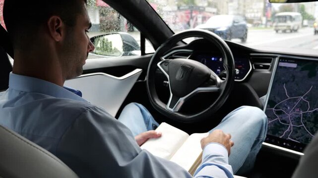 Male businessperson reading book during riding on electrical vehicle with autopilot at rainy day. Successful businessman improving knowledge while ride an autonomous self driving electric car at city