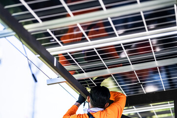 Fototapeta premium A technician in an orange safety jacket working on the wiring and connections of a solar panel system installed on a steel carport structure. The worker is focused on maintenance or installation.
