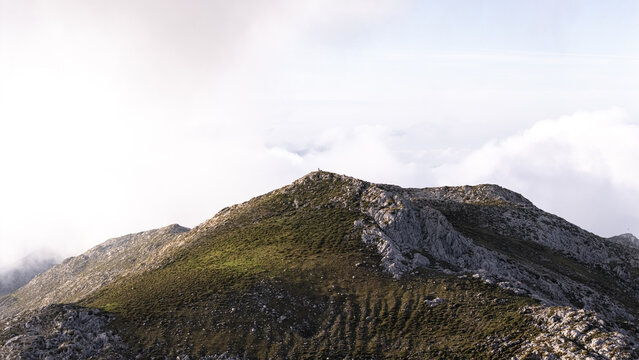 Aerial view of the rugged, rocky peak piercing through a sea of fluffy clouds, a serene landscape of contrasting textures and ethereal light, Picos de Europa, Asturias, Spain.