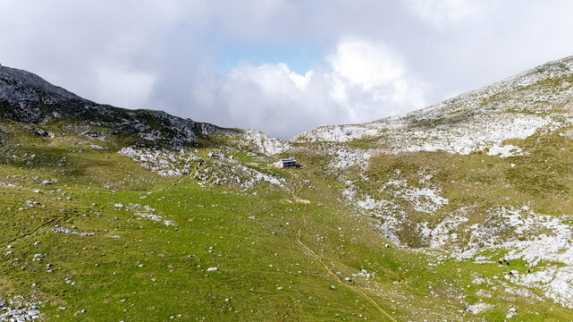 Aerial view of a small building nestled in the Picos de Europa mountains, where the green grass meets the white rocks under a cloudy sky, Picos de Europa, Asturias, Spain.