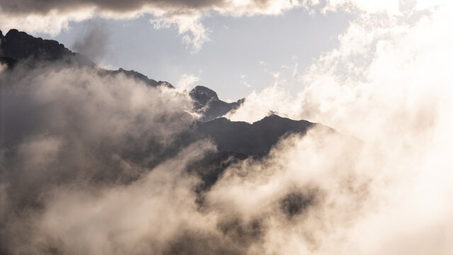 Aerial view of jagged peaks piercing a sea of ethereal clouds, a dance of light and shadow over the rugged terrain, Picos de Europa, Asturias, Spain.