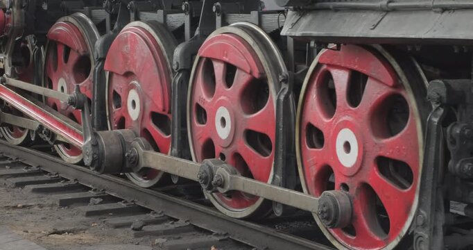 A genuine vintage steam locomotive passes by the camera along the railroad tracks. The levers of the drive mechanism are working, the wheels are turning, and the rails, sleepers, and steam are visible