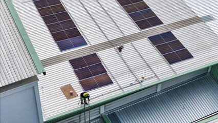 Fototapeta premium technician in safety gear inspects solar panels on a metal rooftop, holding a tool. The scene emphasizes renewable energy, solar technology, and maintenance of sustainable infrastructure.