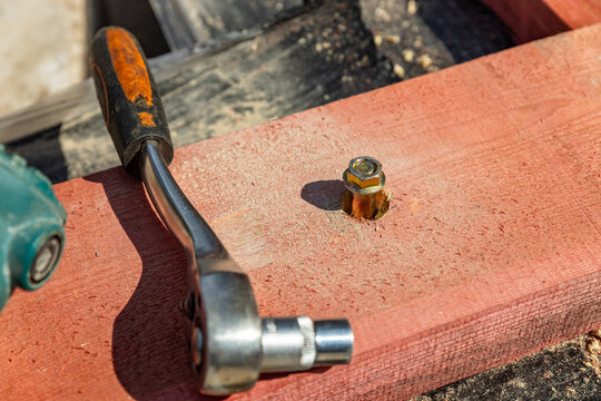 Ratchet socket wrench is used to tighten bolt during outdoor assembly by outdoor. Men is using a ratchet wrench to tighten a bolt in the wood.
