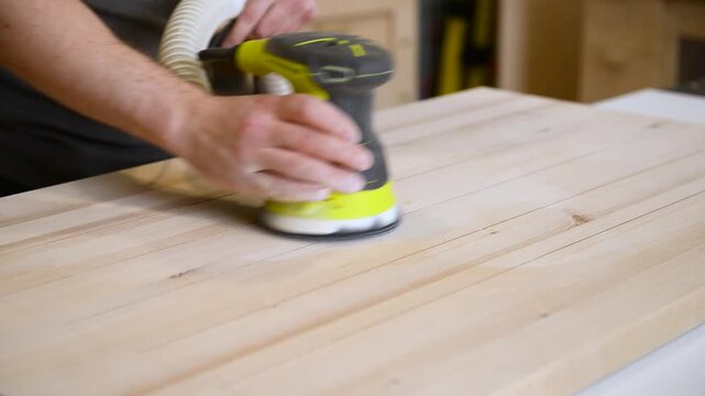 Professional cabinet maker sanding a wooden board with a orbital sander to achieve a smooth surface before applying varnish or oil.