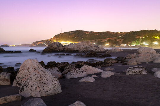 Large granite rocks and dark volcanic sand define the rugged coastline of the coastal village of Matanzas in Chile.