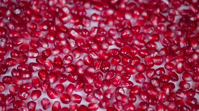 Fresh pomegranate seeds displayed with soft lighting and texture. Close examination of glossy pomegranate arils against plain white surface with gentle lighting