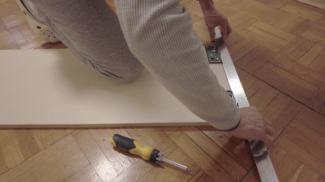 Ruler final check with kneeling hands aligning bracket and panel, screwdriver resting on parquet while installer verifies smooth travel and consistent gap, concluding diy