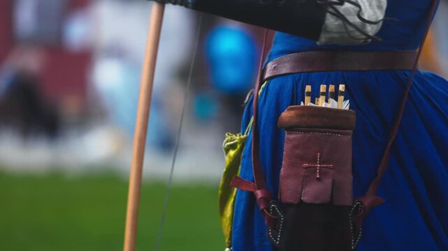 Medieval archery tournament in a castle yard with a woman shooting an arrow from a wooden bow in slow motion. Female archer in traditional medieval dress during historical reenactment, outdoor scene w