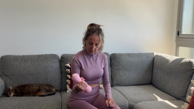 Mujer sentada en el sof&aacute; levantando mancuerna rosa